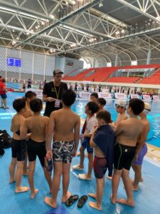 A coach addresses a group of young swimmers by the poolside at OCBC Aquatic Centre. The swimmers listen attentively as they prepare for their next event.